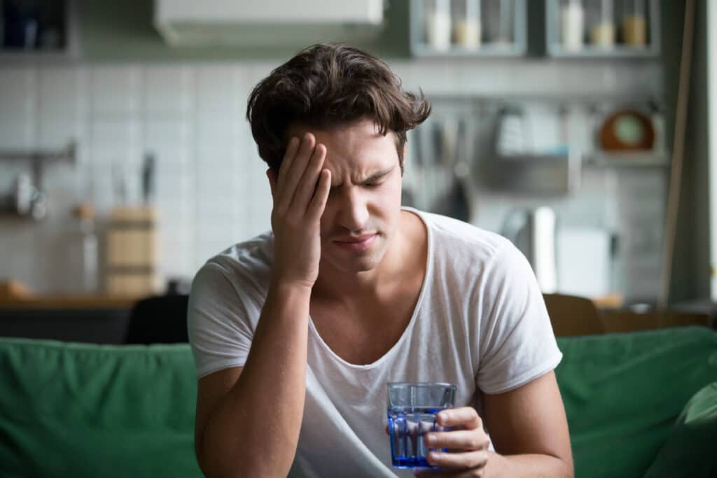 Young man rubbing his head holding a glass of water for headache pain