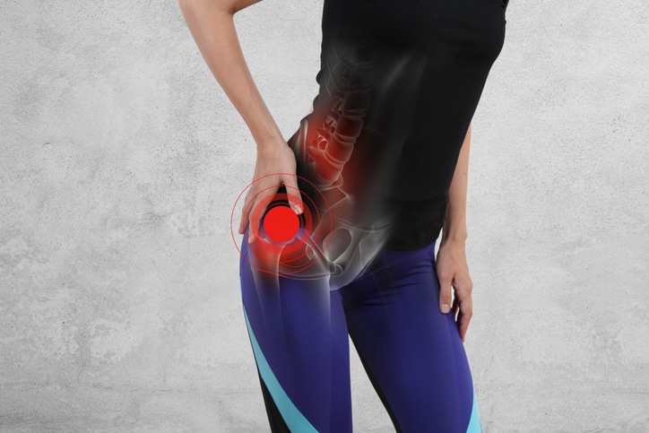 Hip Replacement A person in athletic wear holding their hip with a highlighted red area and an overlay of a hip joint and spine, indicating pain or injury.