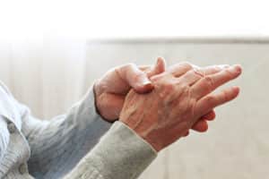 Elderly woman applying moisturizing lotion cream on hand palm easing aches.