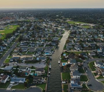 Aerial view of a suburban neighborhood with houses, roads, and green spaces near a beach and coastline during daytime.
