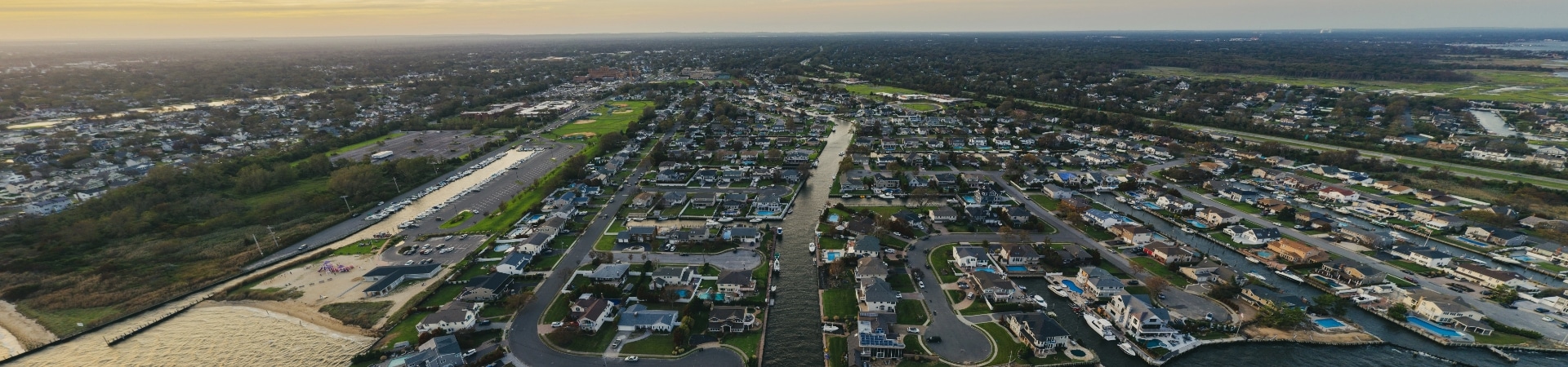 Aerial view of a suburban neighborhood with houses, roads, and green spaces near a beach and coastline during daytime.