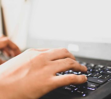 Close-up of hands typing on a black laptop keyboard with a bright screen in the background—a common activity that, when done for long periods, can increase the risk of Carpal Tunnel Syndrome.