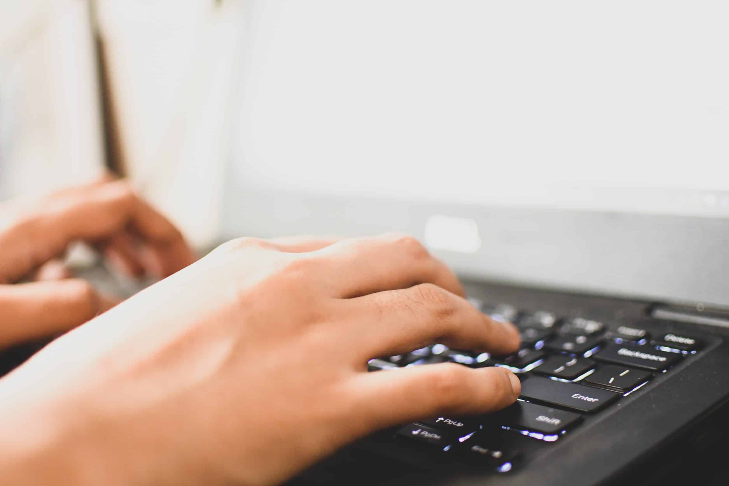 Close-up of hands typing on a black laptop keyboard with a bright screen in the background—a common activity that, when done for long periods, can increase the risk of Carpal Tunnel Syndrome.