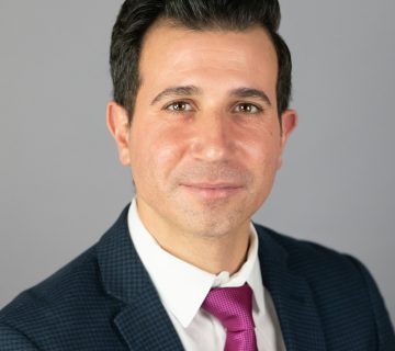 Person in a suit with a pink tie against a plain background, looking at the camera.