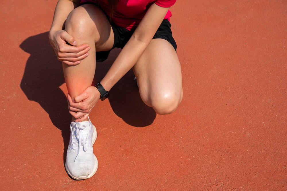 Woman on running track, holding her leg from shin splint pain