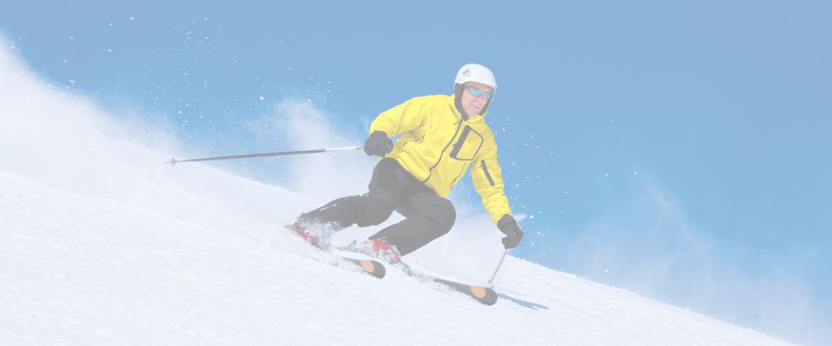 A person wearing a yellow jacket and helmet is skiing downhill on a snowy slope under a clear blue sky.