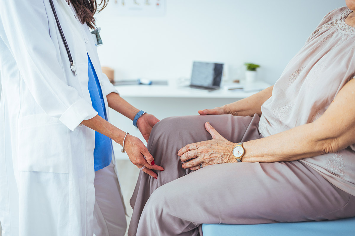 Photo of senior woman having some knee pain. She's at doctor's o A doctor examines an older woman's knee during a medical consultation in a clinic office.