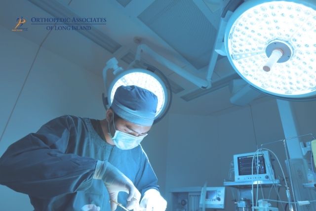 OALI LP (17) A surgeon wearing a mask and surgical cap operates under bright surgical lights in a hospital operating room with medical equipment nearby