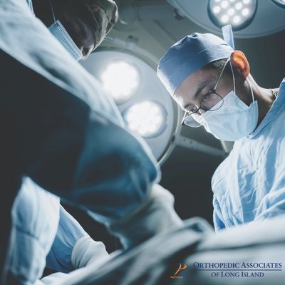 OALI LP (22) Two surgeons in scrubs and masks perform a procedure under bright operating room lights "Orthopedic Associates of Long Island" logo is visible in the corner