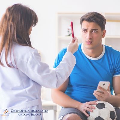 OALI LP (27) A doctor holds a pen up in front of a seated man in a blue shirt holding a soccer ball, conducting an eye or concussion test