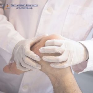 OALI LP (30) A medical professional wearing gloves examines a patient's knee The logo "Orthopedic Associates of Long Island" is visible in the upper left corner