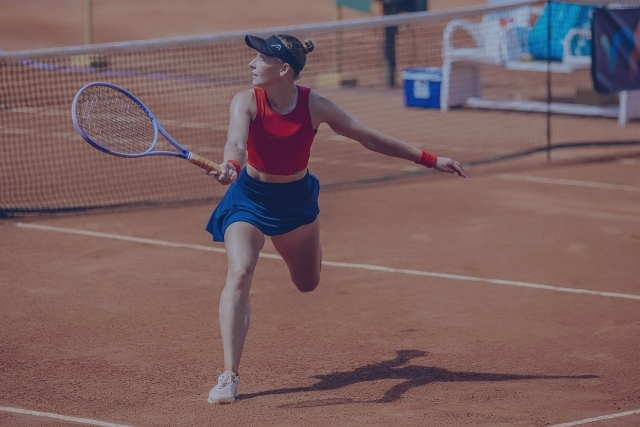 Sports Medicine Doctor in Deer Park A tennis player in a red top and blue skirt swings her racket on a clay court